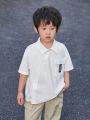 SHEIN Young Boy Casual Loose Fit Short Sleeve Shirt With English Text, Woven Tape Decoration, And Patch Pocket